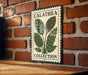 A metal sign with a plant illustration and the text "CALATEA COLLECTION" is displayed on a brick wall.
