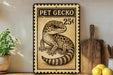 A metal sign with a gecko illustration and the text "PET GECKO 25¢" is displayed on a wooden shelf, accompanied by a potted plant, a wooden cutting board, and some lemons.
