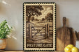 a framed illustration of a wooden gate with a pastoral landscape in the background, placed on a shelf next to a wooden cutting board and a potted plant.