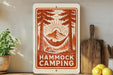 a sign with a hammock and camping scene, surrounded by various kitchen utensils and a potted plant.