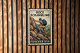 A vintage-style metal stamp with the text "ROCK SCRAMBLING" and "FREVER USA" printed on it, mounted on a wooden wall.