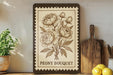A framed illustration of a peony bouquet is displayed on a shelf, accompanied by a wooden cutting board, a potted plant, and some lemons.