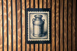 a black and white illustration of a milk can, which is mounted on a wooden wall.