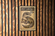 A metal sign with a gecko on it, mounted on a wooden wall.