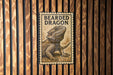 A framed image of a bearded dragon is displayed on a wooden wall.