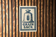 A metal sign with a graphic of a bag of grain and the text "GRAIN SACK" is displayed on a wooden wall.