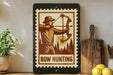 A framed image of a man holding a bow and arrow, with the text "BOW HUNTING" below the illustration, is displayed on a shelf next to a wooden cutting board and a potted plant.