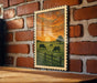 A framed painting depicting a serene rural scene with cows grazing in a field, set against a backdrop of a vibrant sunset sky.