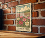 A metal sign with a floral design hangs on a brick wall, depicting a field of flowers.