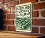 A sign for a "Seedling Nursery" is displayed on a brick wall, featuring a green and white illustration of a plant growing from a garden bed.