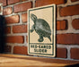 A sign with a turtle illustration on it is mounted on a brick wall.