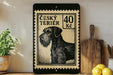 a black and white illustration of a terrier dog, which appears to be a Césky Terrier, on a black and white postage stamp. The stamp is framed with a black border and has the text "Césky Terrier" and "40 Kč" printed on it. The stamp is placed on a wooden surface, and there are some kitchen utensils, such as a knife and a spoon, visible in the background.