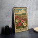 A metal stamp with a floral design, featuring a field of flowers and mountains in the background, is displayed on a table.