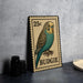 A metal stamp featuring a colorful illustration of a budgie bird, with the text "25c" printed on it.