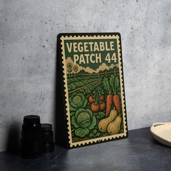 A metal sign with a vintage-style illustration of vegetables and a stamp-like border, placed on a countertop next to some black camera lenses.