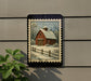 A framed painting of a red barn with a snowy landscape in the background is displayed on a wall, with a plant to the left.