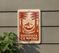 A sign with a hammock and camping scene is mounted on a wall, with a plant to the left.