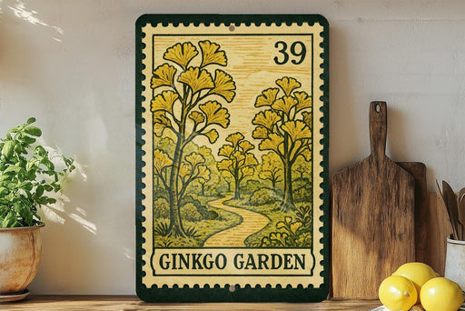 a framed print of a garden scene with a path leading through it, surrounded by yellow flowers and greenery. The print is framed in a green border and has the text "GINKGO GARDEN" printed on it. The print is displayed on a shelf next to a wooden cutting board and a potted plant.