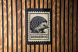 A black and white stamp-like sign with a hedgehog illustration on it, mounted on a wooden wall.