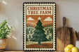 A Christmas tree farm sign with a pine tree and mountains in the background, placed on a wooden shelf next to a wooden cutting board and a potted plant.