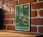 A metal sign with a postage stamp design hangs on a brick wall, depicting a water garden scene with lily pads and a bridge.