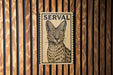 A wooden wall with a framed image of a spotted cat, which appears to be a serval cat, mounted on it.