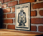 A metal sign with a lantern illustration is mounted on a brick wall.