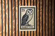 A barn owl postage stamp is displayed on a wooden wall.