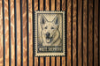 A metal sign featuring a close-up of a white shepherd dog's face, mounted on a wooden wall.