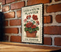 A vintage-style metal sign with a floral illustration of geraniums, mounted on a brick wall.