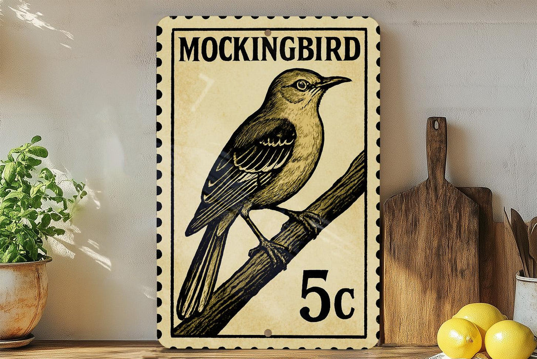 A vintage-style postage stamp featuring a detailed illustration of a bird perched on a branch, with the text "MOCKINGBIRD" and the denomination "5c" printed on it. The stamp is displayed on a shelf next to a wooden cutting board and a potted plant.