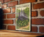 A framed print of a postage stamp depicting a lavender plant is displayed on a brick wall.