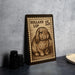 A wooden postcard or stamp featuring a rabbit, placed on a table next to some black camera lenses.