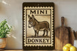 a wooden sign with a donkey illustration, placed on a shelf next to a wooden cutting board and some lemons.