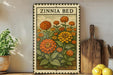 A vintage-style metal sign with a floral illustration of a garden bed, featuring a variety of orange and yellow flowers, is displayed on a shelf next to a wooden cutting board and a potted plant.