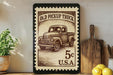 a framed stamp-like artwork depicting an old pickup truck, placed on a shelf next to a wooden cutting board and some lemons.