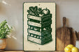 a wooden crate with a stack of green crates on top, containing various fruits and vegetables, such as apples and oranges. The crate is placed on a wooden surface, and there are some potted plants and kitchen utensils visible in the background.