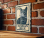 A metal sign featuring a black and white illustration of a cat, mounted on a brick wall.