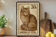 a framed stamp-like artwork depicting a cat, with the text "AMERICAN CURL" printed on it. The artwork is displayed on a shelf next to a wooden cutting board and a potted plant.
