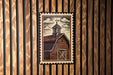 A framed illustration of a barn with a steeple is displayed on a wooden wall.