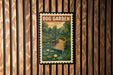 A vintage-style postage stamp depicting a wooden bridge over a pond with lily pads, hanging on a wooden wall.