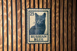 A blue and white postage stamp featuring a cat, with the text "RUSSIAN BLUE" printed on it, is displayed on a wooden wall.
