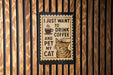 A sign with the text "I JUST WANT TO DRINK COFFEE AND PET MY CAT" is displayed on a wooden wall.