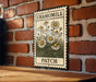 A metal sign with a floral design hangs on a brick wall, displaying the word "CHAMOMILE" and "PATCH".