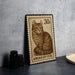 A wooden postcard featuring an illustration of a cat, with the text "AMERICAN CURL" printed on it, is displayed on a table next to some black camera lenses.