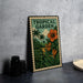 A metal sign with a tropical garden theme, featuring palm trees, flowers, and lush foliage, is displayed on a table.