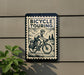 a sign that reads "Bicycle Touring" with a bicycle illustration, mounted on a wall next to a plant.