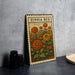 A metal sign with a floral design, featuring a variety of colorful flowers, is displayed on a table.