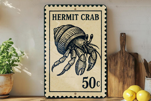 A vintage-style metal sign featuring a hermit crab, with the text "HERMIT CRAB" and "50c" printed on it. The sign is placed on a wooden surface, with a potted plant, a wooden cutting board, and some lemons nearby.