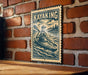 A vintage-style metal sign with a kayaker illustration is mounted on a brick wall.